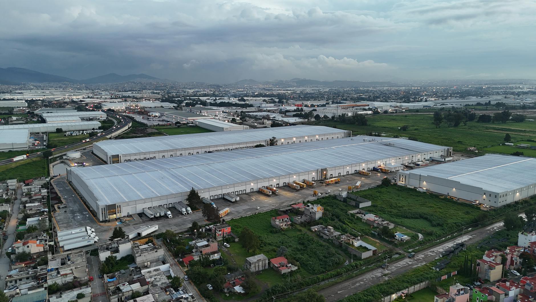 Aerial view of industrial warehouses in Mexico City surrounded by residential areas and greenery.